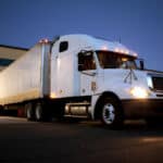 A white semi truck is parked at a shipping center at night, highlighting the National Truck Driving Championship's focus on safety.