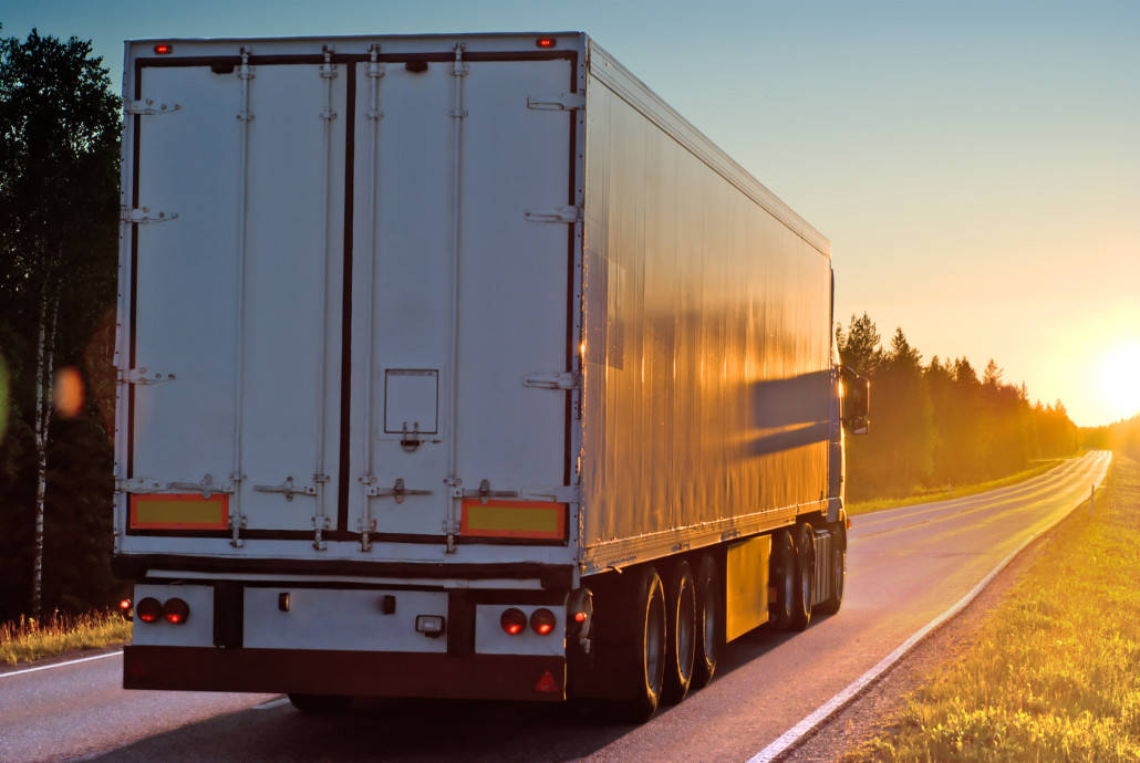 Semi truck driving down a highway into the sunset